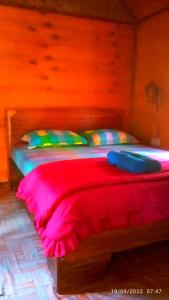 Cama con manta roja y almohadas coloridas en Ariel Bungalow Tetebatu, en Tetebatu