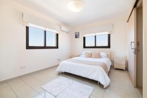 a white bedroom with a bed and two windows at Blue Serenity Complex in Larnaka +19 photos