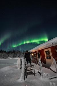 a person sitting on a bench under the northern lights at Hommala Riverside Lodge with Terrace, Sauna & Auroras near Rovaniemi in Raiskio +50 photos