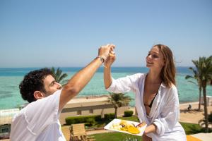 Un uomo e una donna che tengono un piatto di cibo in spiaggia di Sunny Days El Palacio Resort & Spa a Hurghada