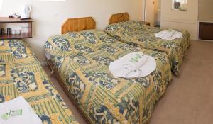 three beds in a hotel room with towels on them at The Swiss Motel in Cooma