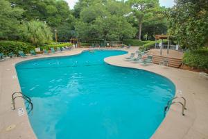 a swimming pool with blue water and chairs and trees at Turnberry Village in Hilton Head Island