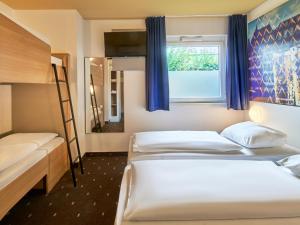 a bedroom with two beds and a window with blue curtains at B&B Hotel Frankfurt-Nord in Frankfurt/Main