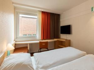 a hotel room with two beds and a desk and a window at B&B Hotel Duisburg Hbf-Nord in Duisburg