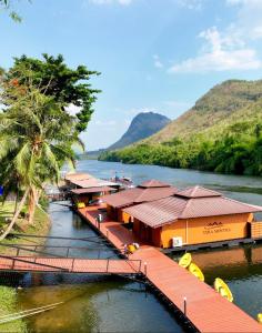 a group of buildings on a river with mountains in the background at ธารามนตรา รีสอร์ท (Taramontra resort) in Tha Kradan