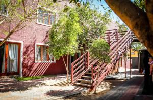 una escalera de madera que conduce a un edificio rosa con árboles en Windhoek Gardens Boutique Hotel en Windhoek