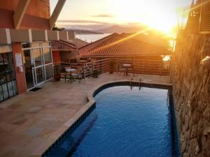 a swimming pool in front of a house with the sunset at Jurerê Ocean Flats in Florianópolis