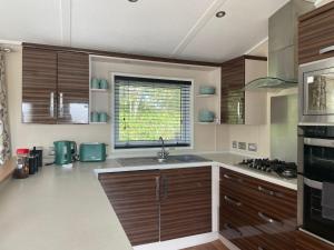 a kitchen with wooden cabinets and a sink and a window at 3 Bedroom Lodge - Willows 24, Trecco Bay in Newton