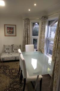 une salle à manger avec une table en verre et des chaises blanches dans l'établissement Leamington Park Studio with Parking, à Londres