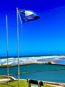 uma bandeira azul e branca e um banco ao lado do oceano em COCOVIEW BEACH HOUSE em Southbroom