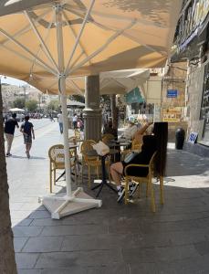 a woman sitting in chairs under an umbrella on a street at La Provençale in Jerusalem