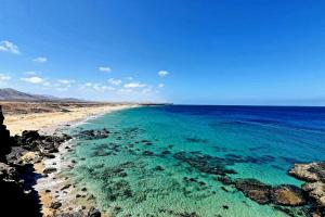 a beach with turquoise water and rocks at Casa Abuelo Antonio in El Cotillo
