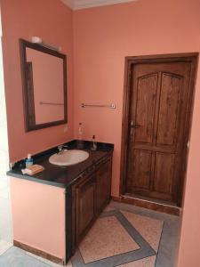 La salle de bains est pourvue d'un lavabo, d'un miroir et d'une porte. dans l'établissement Belles appartements à côté de la plage Tamehrouchte, à Mirleft