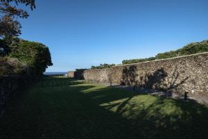 eine alte Steinmauer mit einem Schatten auf dem Gras in der Unterkunft ENTRE MUROS - Turismo Rural - Casa com jardim e acesso direto ao mar in Ribeira Grande