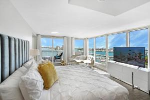a white bedroom with a large bed and a tv at The Palms! Direct water view corner condo in Miami