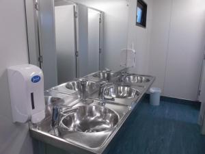 a row of stainless steel sinks in a bathroom at Hampshire Holiday Parks - Arrowtown in Arrowtown