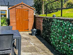 cobertizo de madera con puerta de madera junto a un seto en Thistle Cottage, en Portpatrick