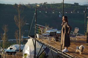 a woman standing on a dock with two dogs at Đamb'ri Top View Farmstay & Glamping in Bao Loc