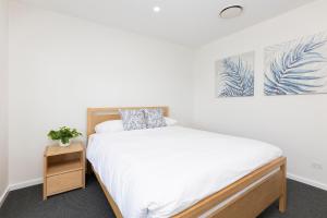 - une chambre avec un lit doté de draps blancs et d'une plante dans l'établissement Palm Breeze, à Forster