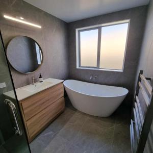 La salle de bains est pourvue d'une baignoire, d'un lavabo et d'un miroir. dans l'établissement Brand new holiday home in Snells Beach, à Snells Beach