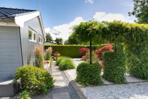 um jardim com arbustos, uma árvore e uma casa em Beautiful 6-person chalet with Finnish wood-fired sauna em Tzummarum