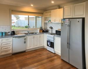 a kitchen with white cabinets and a refrigerator at OCEAN BREEZE in Warrnambool