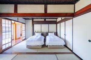 two beds in a room with windows at 佐渡古民家ステイ さどまり -Sadomari Historical Villa- in Sado