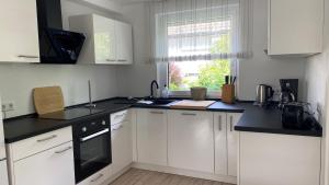 Ferienwohnung Lilienthal في Lilienthal: مطبخ بخزائن بيضاء وطاولة عمل سوداء +7 صور