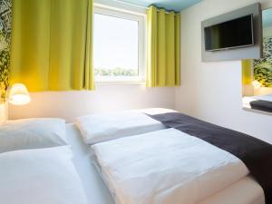1 dormitorio con 2 camas, TV y ventana en B&B Hotel Karlsruhe en Karlsruhe