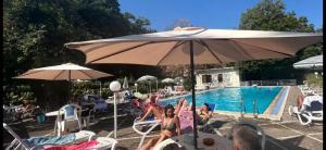 um grupo de pessoas sentadas sob um guarda-chuva perto de uma piscina em Mondial Park Hotel em Fiuggi