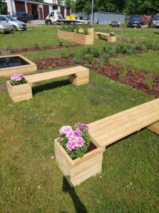 three wooden benches with flowers in the grass at HOMER Bydgoszcz Ośrodek Rehabilitacji i Szkolenia PZN in Bydgoszcz