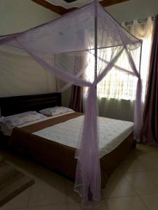 ein Schlafzimmer mit einem Himmelbett und einem Fenster in der Unterkunft Olive Palm Suites Jinja in Jinja