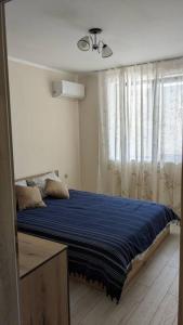 a bedroom with a bed with blue sheets and a window at Сарафово Център in Burgas City