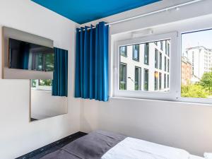 1 dormitorio con cortinas azules, 1 cama y ventana en B&B Hotel Hamburg City-Ost, en Hamburgo