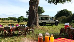 een tafel en stoelen en een busje geparkeerd naast een boom bij Muthu Keekorok Lodge, Maasai Mara, Narok in Keekorok