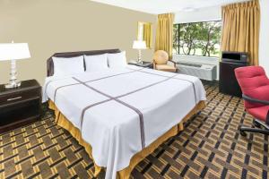 Cette chambre d'hôtel comprend un grand lit et un fauteuil rouge. dans l'établissement Travelodge by Wyndham Shreveport LA, à Shreveport