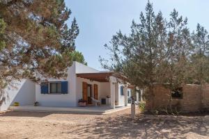 mały biały dom z niebieskimi oknami i drzewami w obiekcie Es Lliri Blanc w mieście Cala Saona