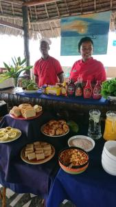 dos hombres sentados en una mesa con platos de comida en Highland Bungalows, en Nungwi