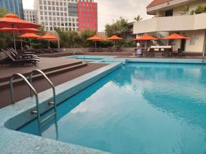 una piscina con sombrillas naranjas, mesas y sillas en The Heritage Hotel Manila, en Manila
