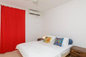 1 dormitorio con cama blanca y cortina roja en Netanyas One Bedroom Beachside Escape, en Netanya