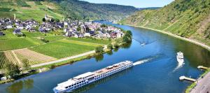 a boat traveling down a river with a town at Mosel Village Resort in Ellenz-Poltersdorf