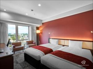 two beds in a hotel room with a red wall at Daiwa Roynet Hotel Fukuyama Ekimae in Fukuyama
