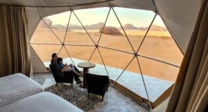dwoje ludzi siedzących w namiocie z widokiem na pustynię w obiekcie Rum Kingdom Camp w mieście Wadi Rum