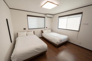 2 Betten in einem kleinen Zimmer mit 2 Fenstern in der Unterkunft トワイライトヒルズ Twilight Hills in Motobu