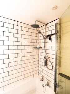 La salle de bains est pourvue de carrelage blanc, d'une douche et d'une baignoire. dans l'établissement Rosecott, à St Ives
