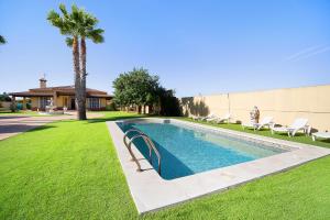 a swimming pool in a yard with chairs and a palm tree at Villa Juani in Chiclana de la Frontera