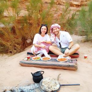 un homme et une femme assis sur la plage avec de la nourriture dans l'établissement Wild Oryx Camp Bubbles, à Wadi Rum
