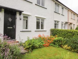 a white house with a black door and some flowers at 1 Millbank in Keswick