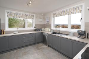a kitchen with gray cabinets and two windows at Glen View in Inverness