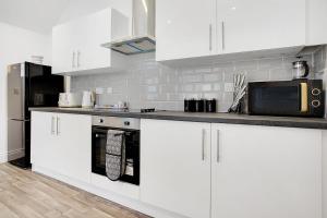 een keuken met witte kasten en een zwarte koelkast bij Spacious & Modern Oasis, 4-Bed House, Sleeps 7 in Sunderland